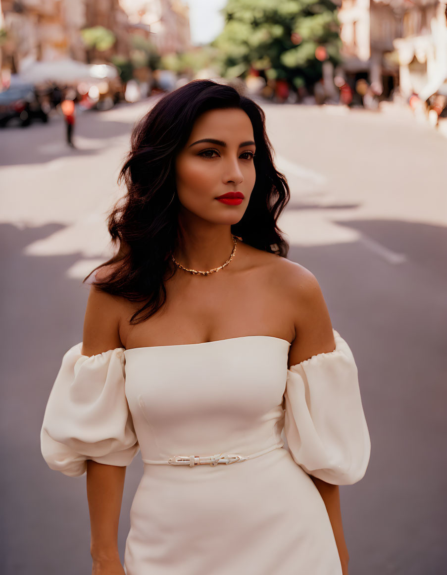 Stylish woman in white off-shoulder dress with gold choker necklace, standing on sunny