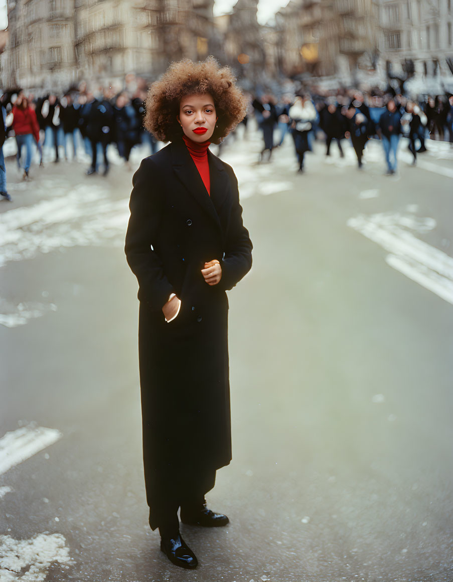 Confident woman with afro in black coat and heels on city street.