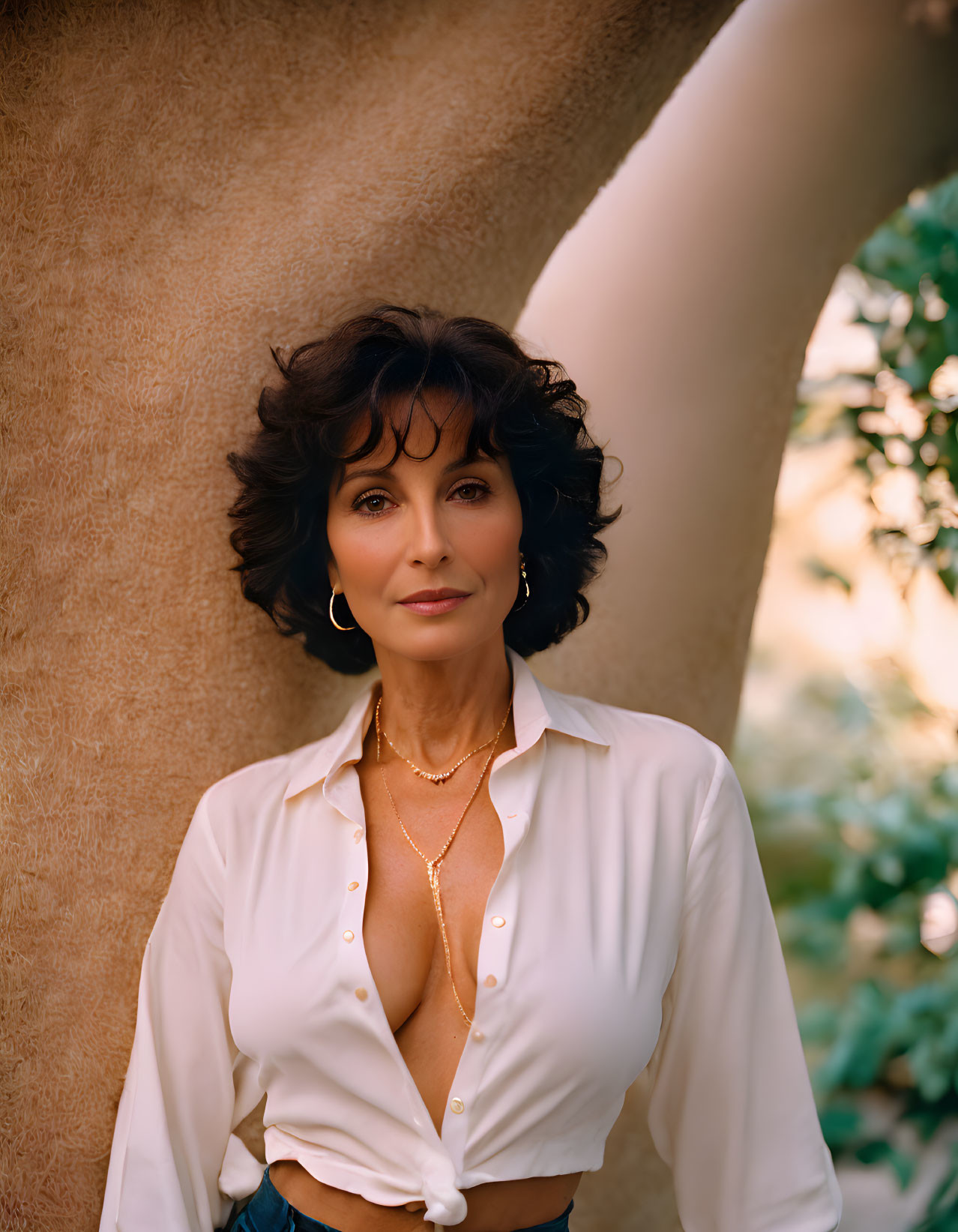 Dark Curly-Haired Woman in White Blouse and Jeans Poses Confidently