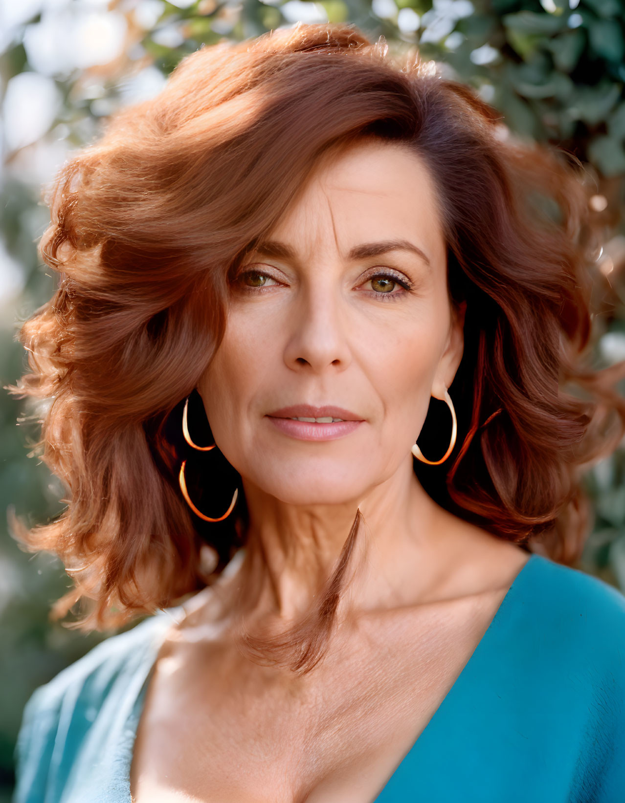 Woman with Auburn Hair and Hoop Earrings in Teal Top against Greenery Background