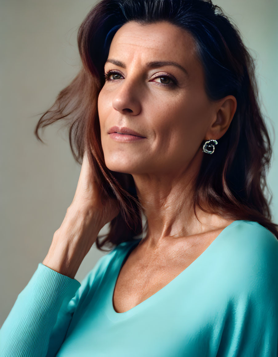 Brown-haired woman in turquoise blouse gazes thoughtfully.