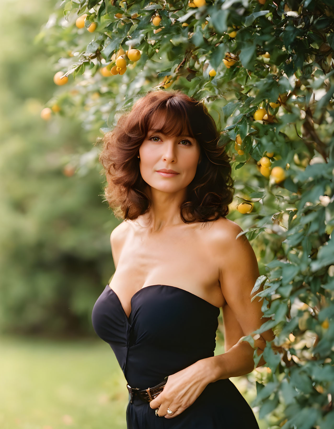 Woman in Strapless Black Dress by Tree with Yellow Fruits in Lush Green Setting