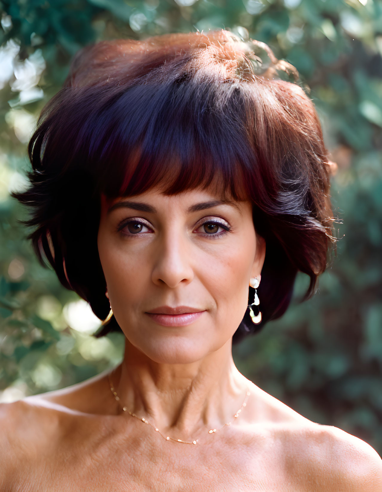 Portrait of woman with short dark hair, purple highlights, earrings, necklace, bare-shouldered outfit