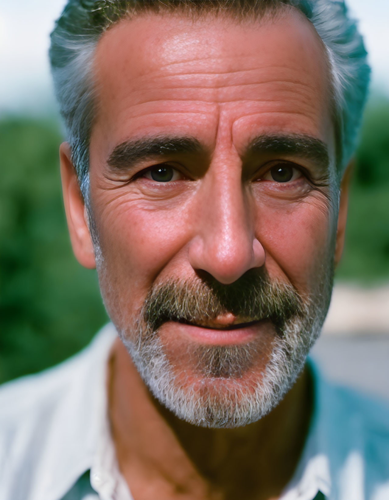 Smiling middle-aged man with gray hair and beard in white shirt on green background