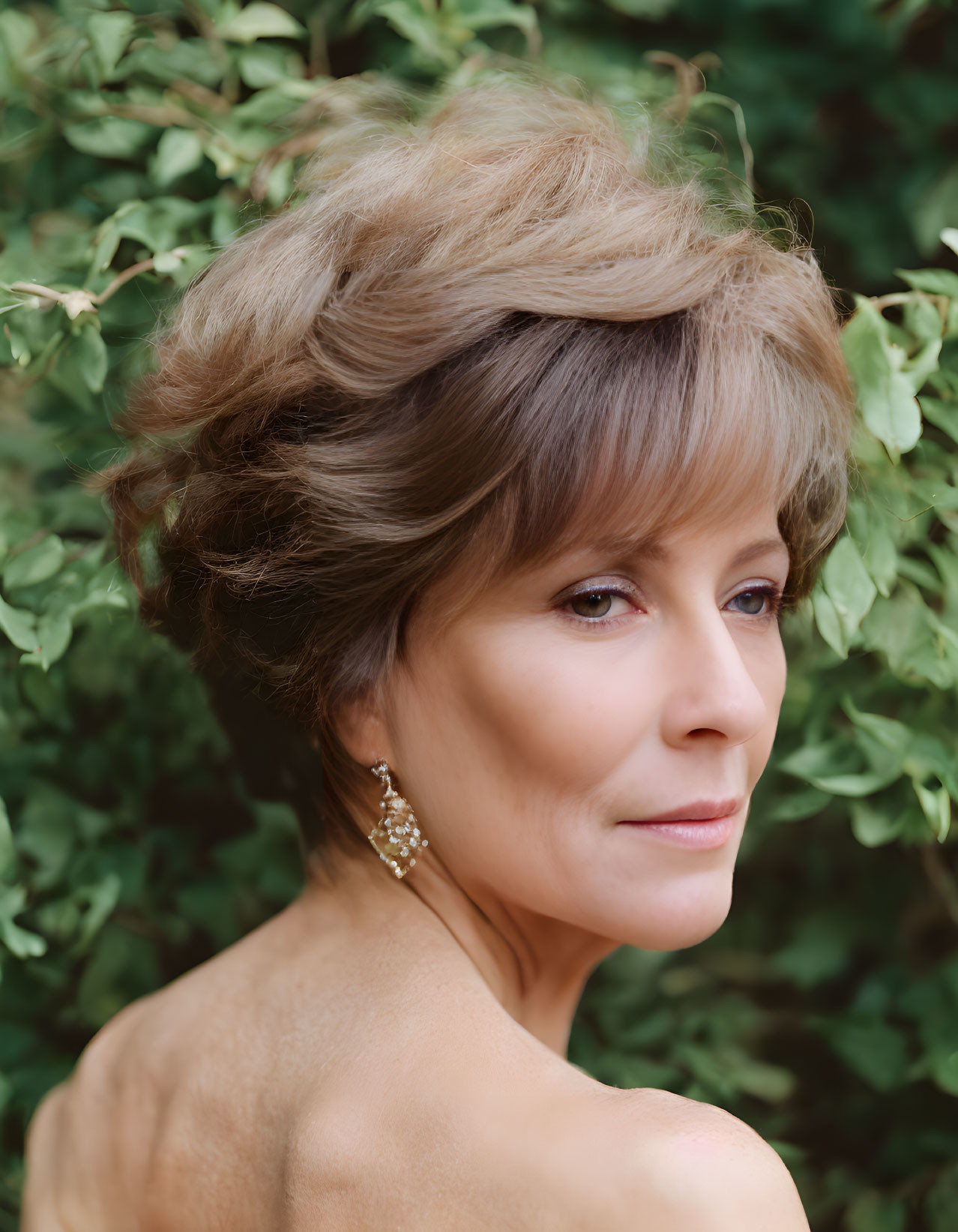 Elegant older woman with styled hair and makeup against green foliage