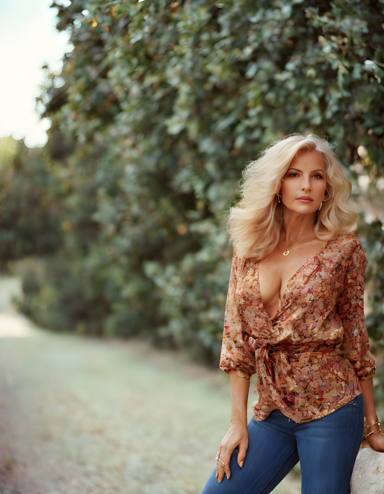 Blonde woman in floral blouse and jeans outdoors.