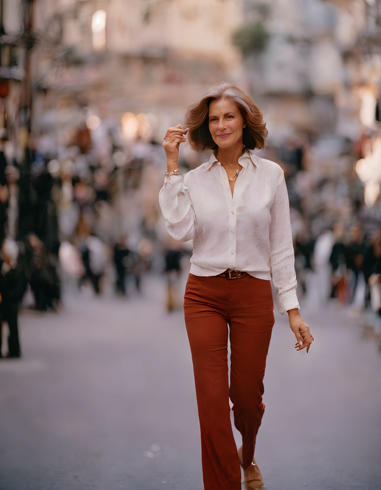 Confident woman in semi-transparent blouse and terracotta pants smiling on busy street