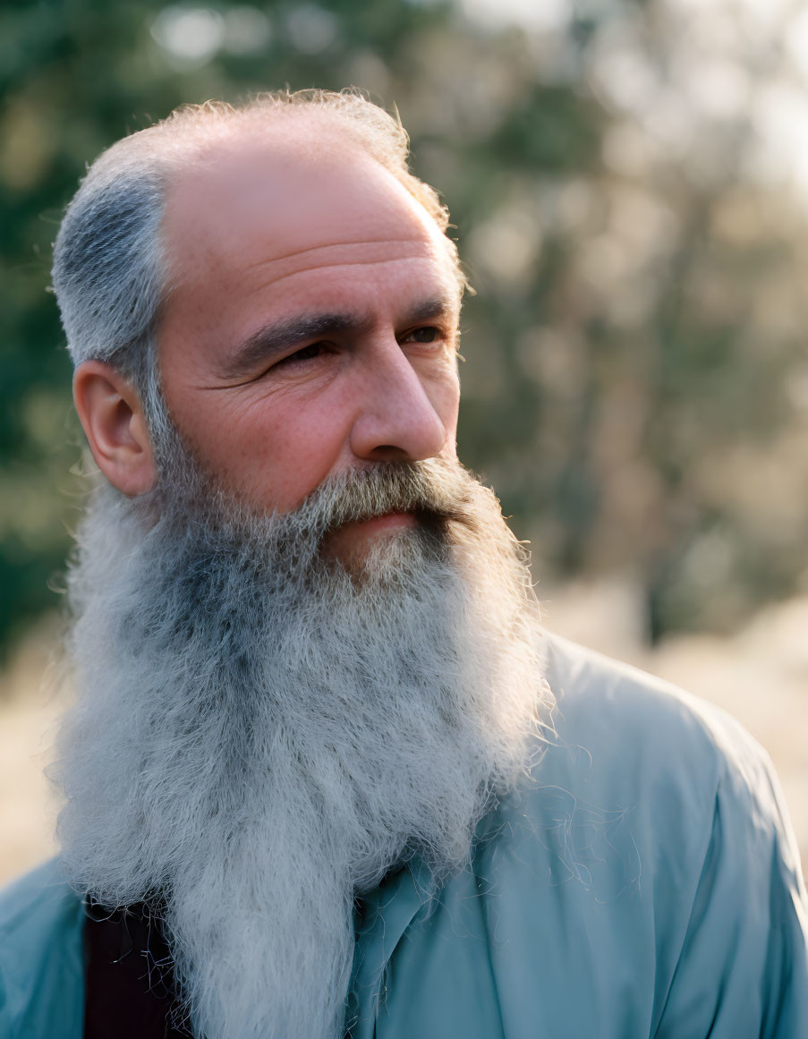 Elderly man with white beard and blue shirt, gazing into the distance.