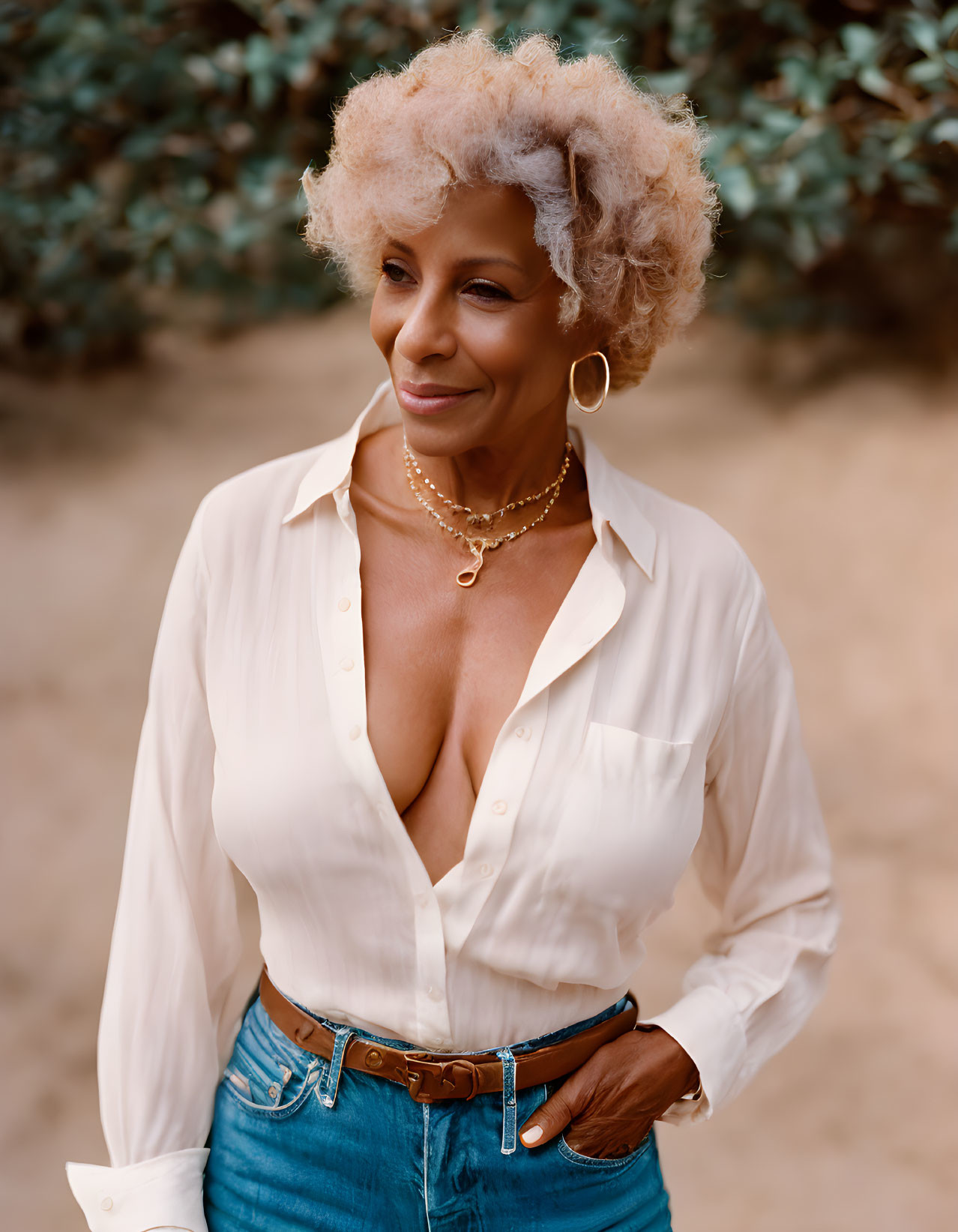 Curly white-haired older woman in white shirt and denim skirt smiling outdoors