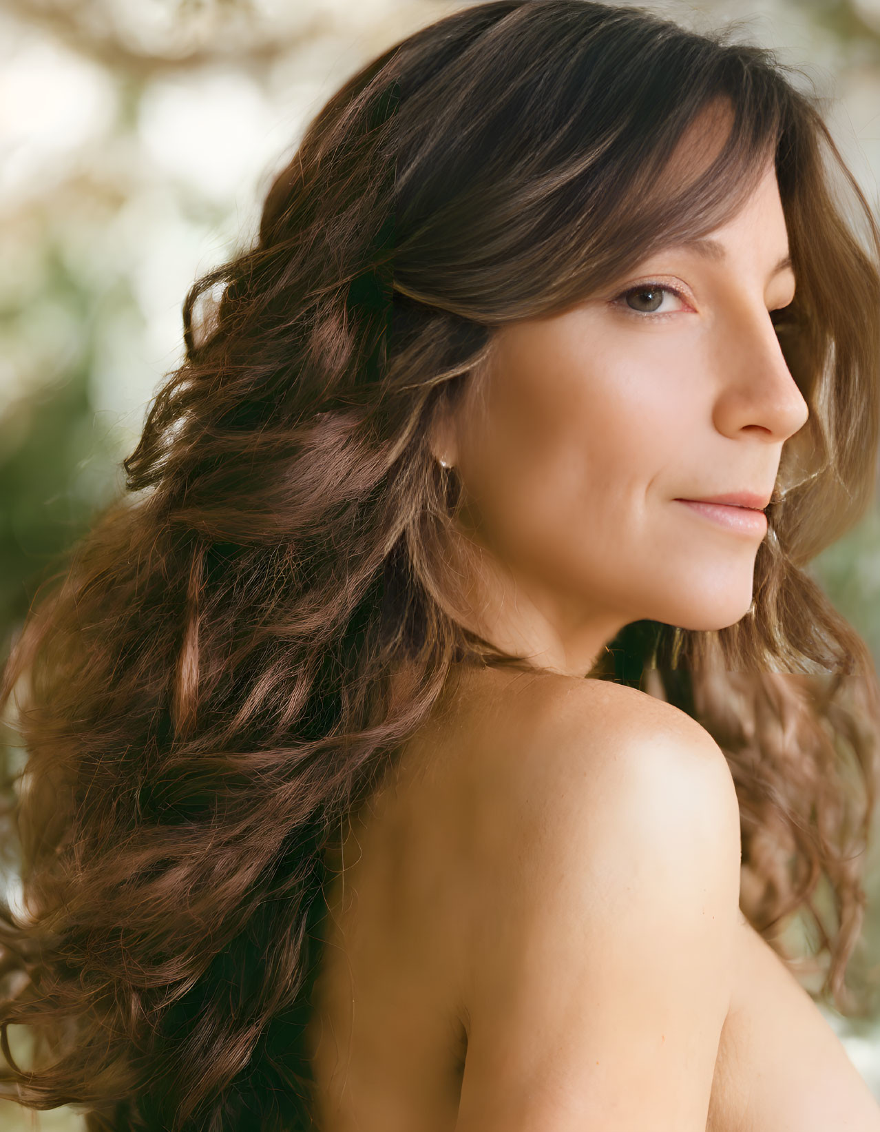 Long wavy brown hair woman with soft smile, bare shoulders, blurred green background