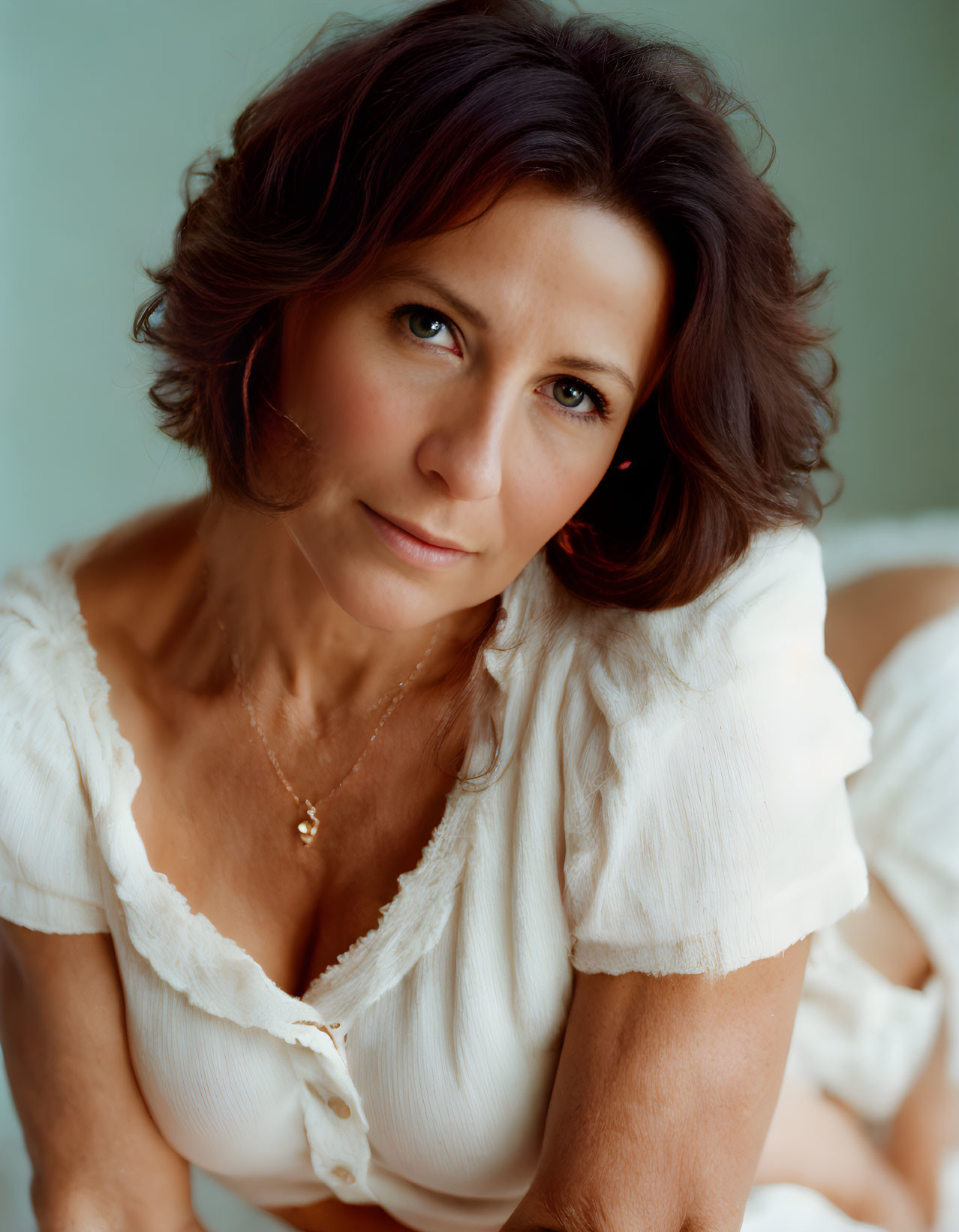 Woman with Brown Hair and Green Eyes in White Blouse on Teal Background