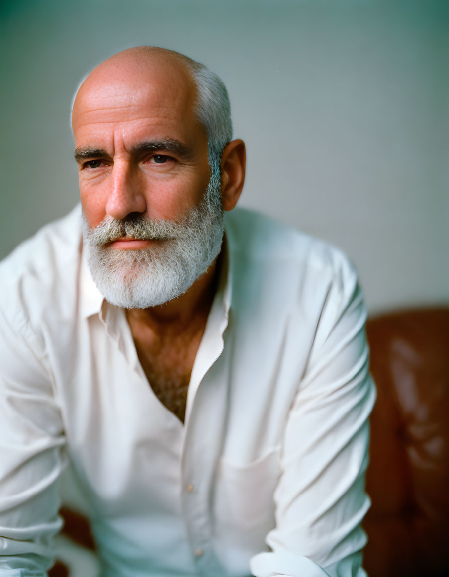 Elderly man with white beard and shirt gazes thoughtfully.