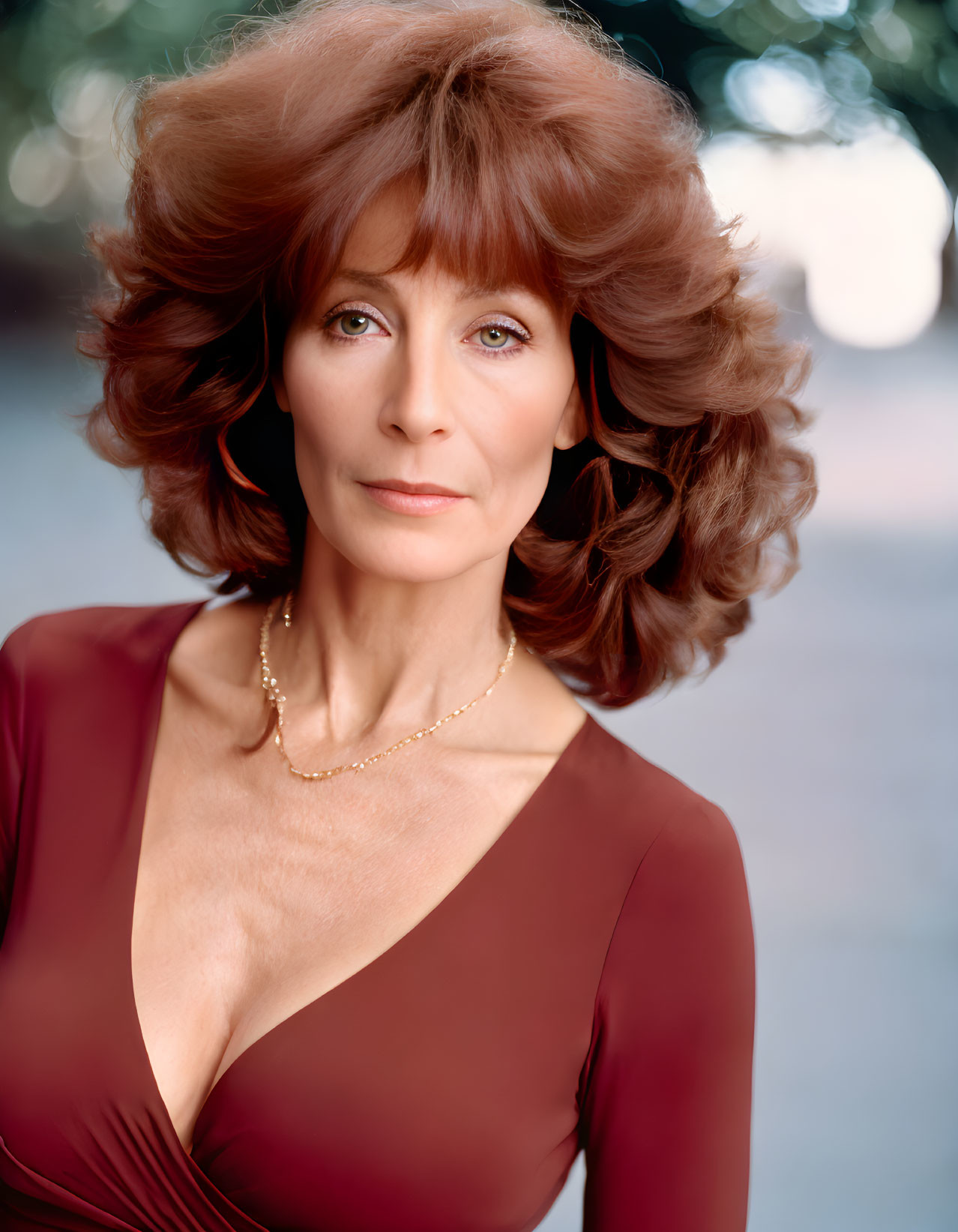 Auburn-haired woman in brown dress with necklace gazes confidently.