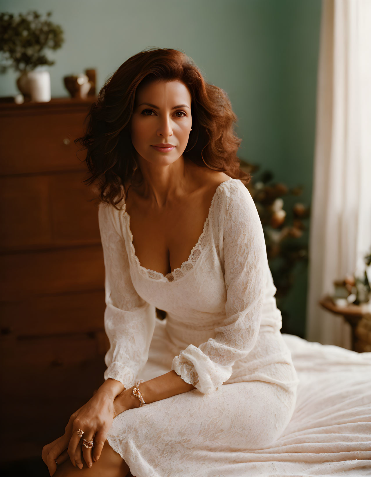 Elegant woman in white lace dress on bed with green wall and warm lighting