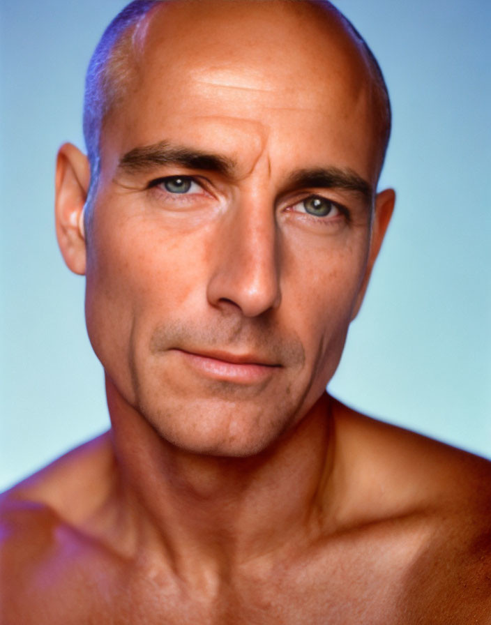 Portrait of bald man with piercing blue eyes and stubble on blue background