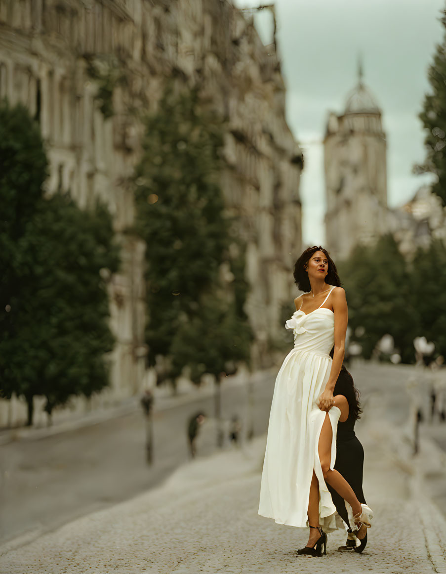 Woman in White Dress Poses in City Street with Classic Architecture