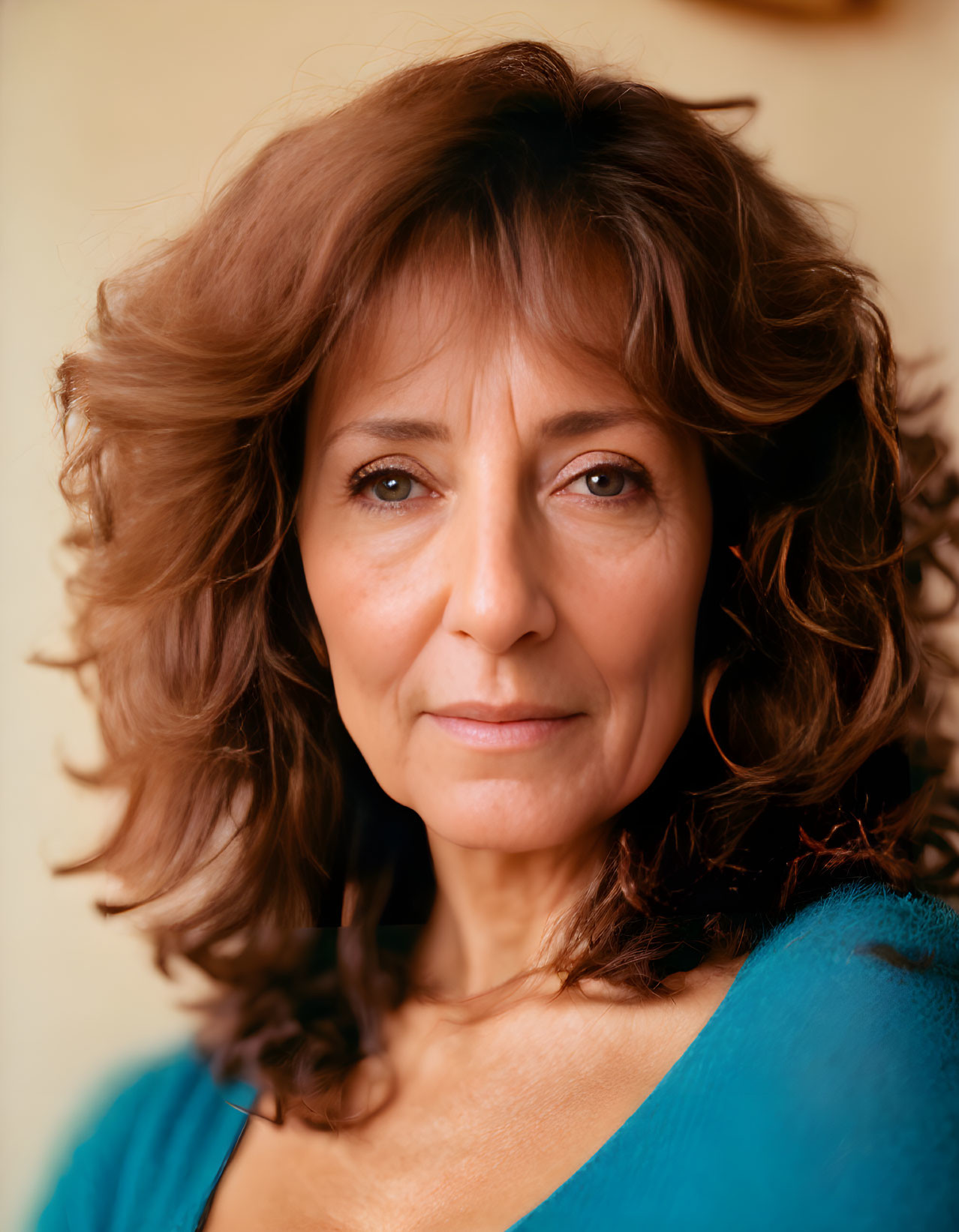 Portrait of woman with curly brown hair and blue top on warm-toned backdrop