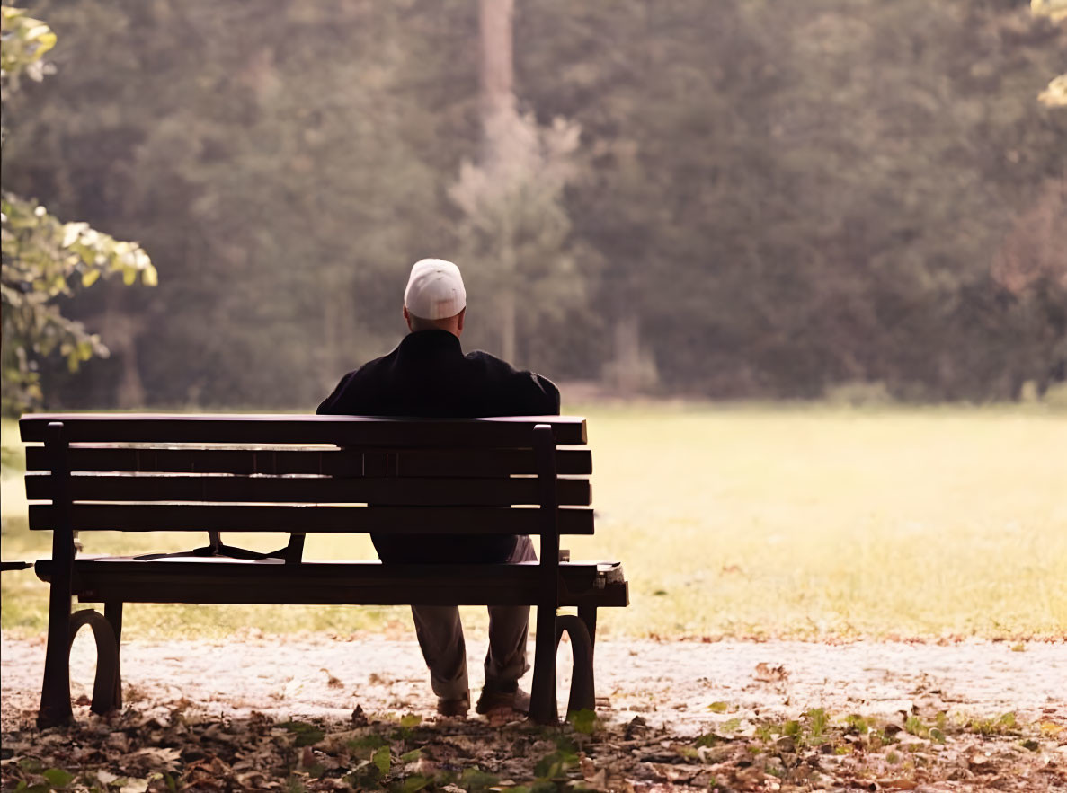 Person in White Cap and Black Outfit Sitting on Park Bench Facing Peaceful Landscape