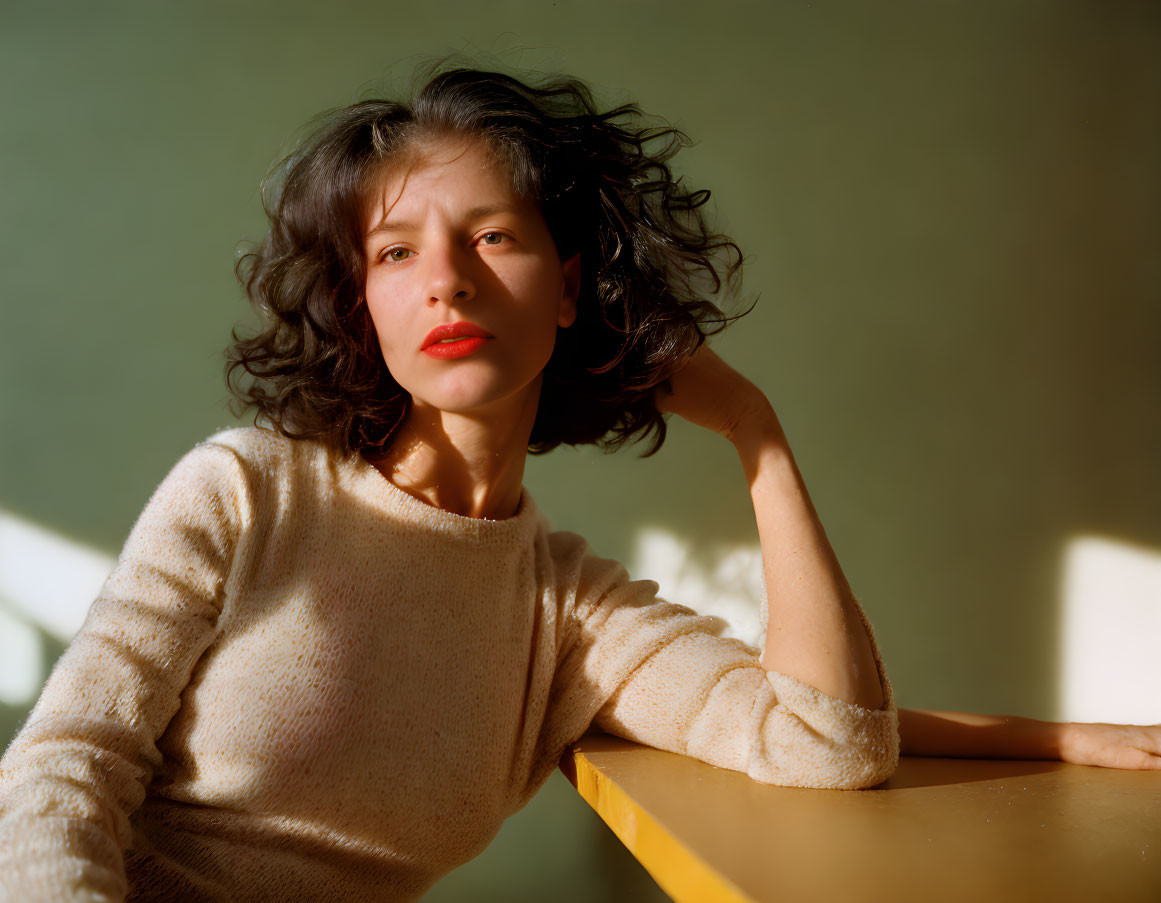 Wavy-haired woman in beige sweater against green backdrop