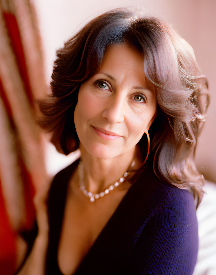 Middle-aged woman with wavy hair in blue top and pearl necklace smiling.