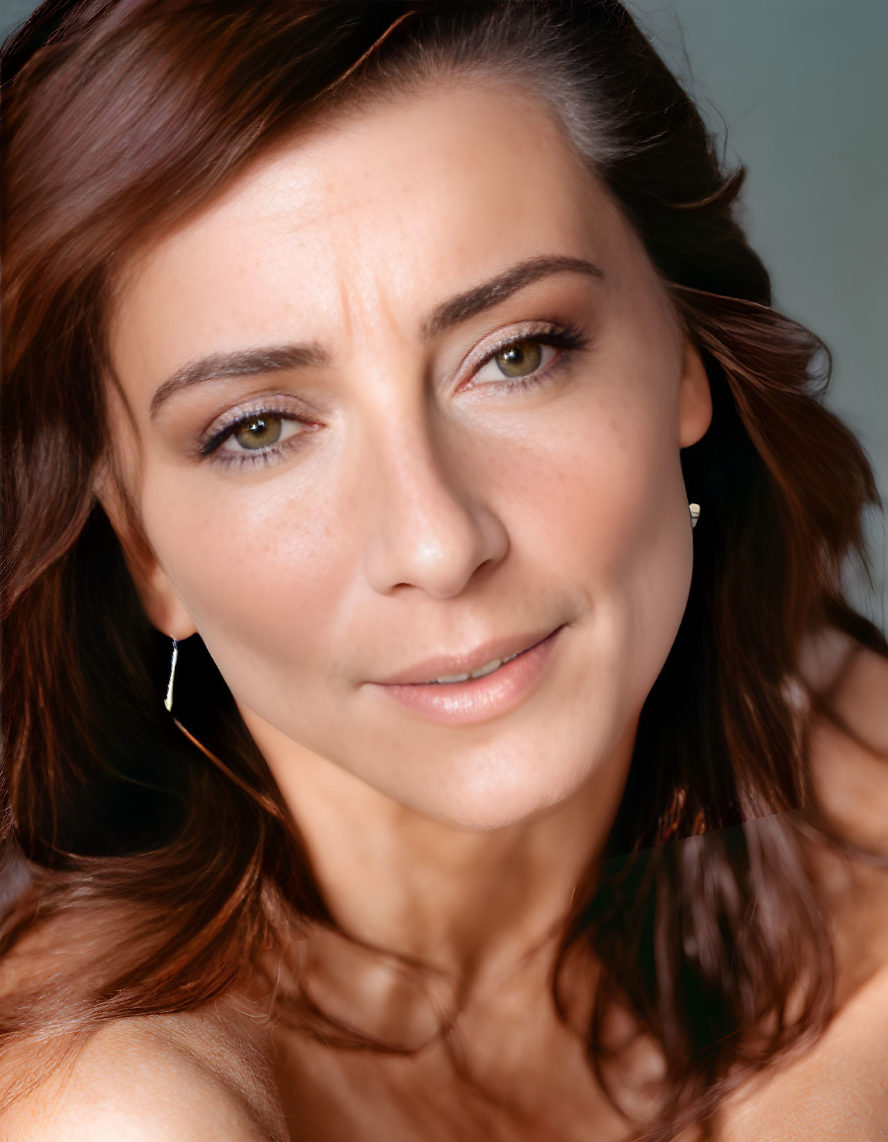 Portrait of woman with brown hair, hazel eyes, and earrings smiling softly