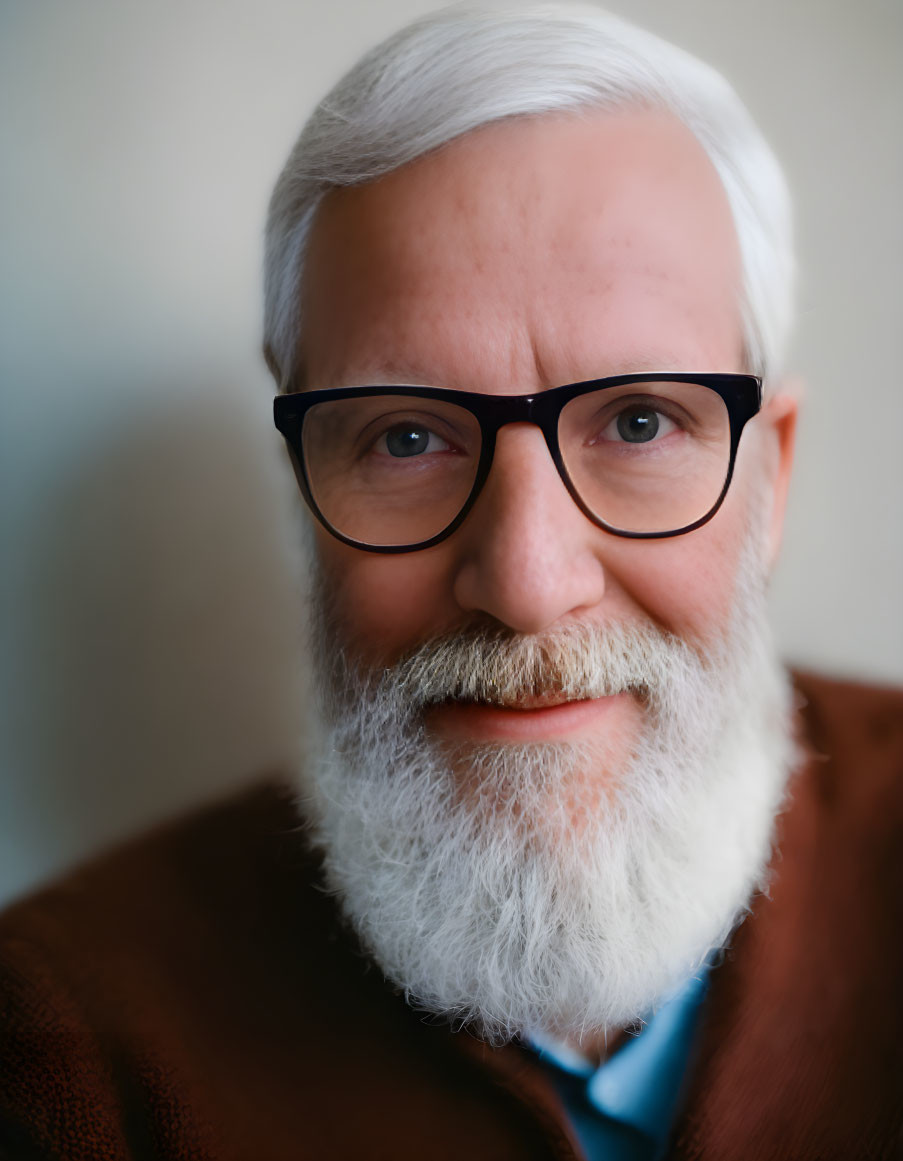 Elderly man with white beard and glasses in brown jacket smiles gently