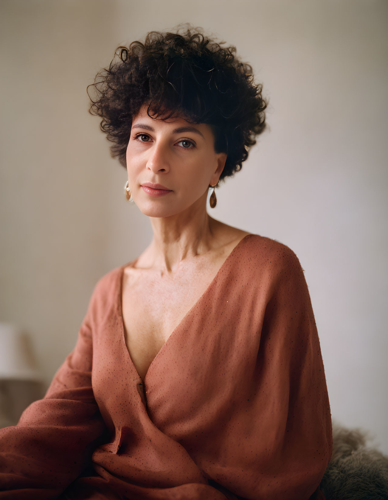 Short Curly-Haired Woman in Rust Blouse Seated with Soft Background