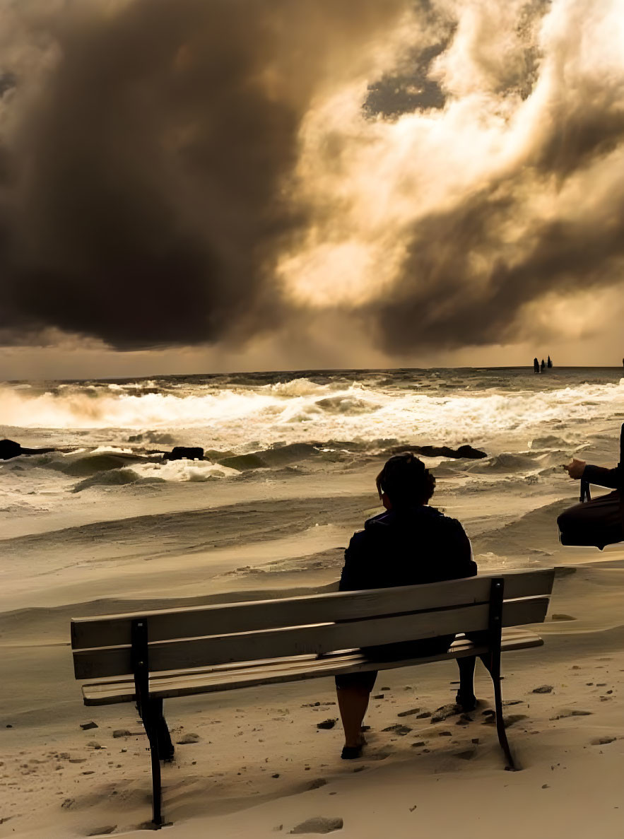 Person sitting on beach bench watching turbulent sea under dramatic sunset sky