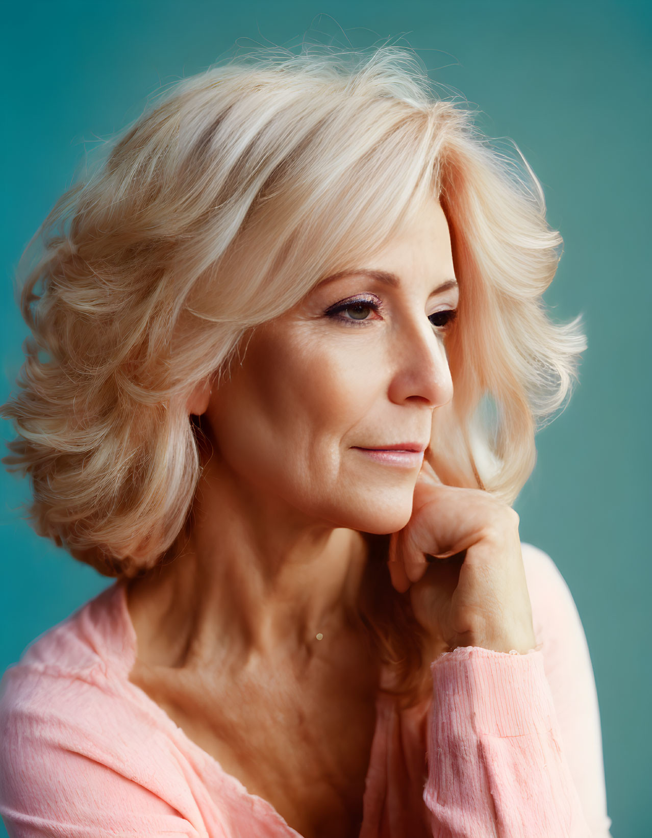 Blonde mature woman portrait in thoughtful pose against teal background