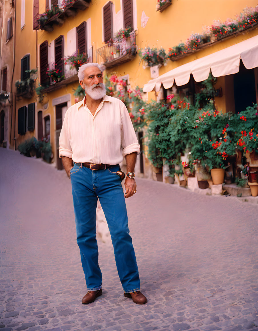 White-bearded older man on cobblestone street with colorful buildings.