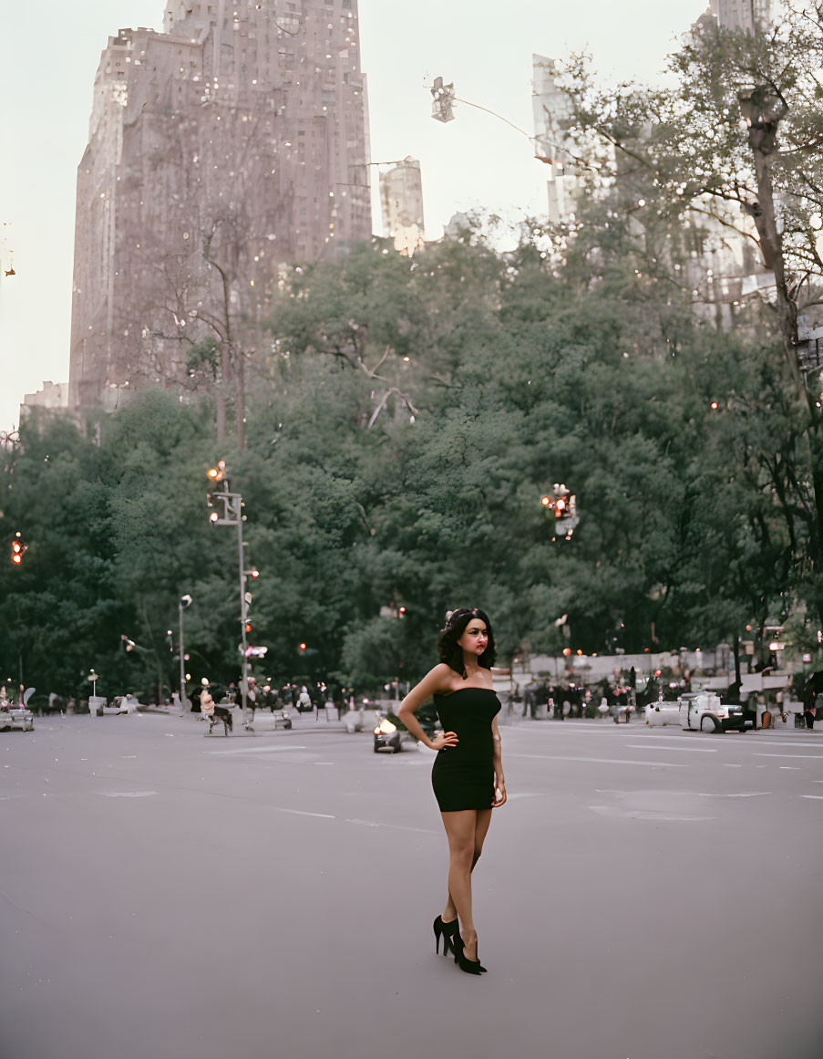 Confident Woman in Black Dress Stands in Urban Plaza