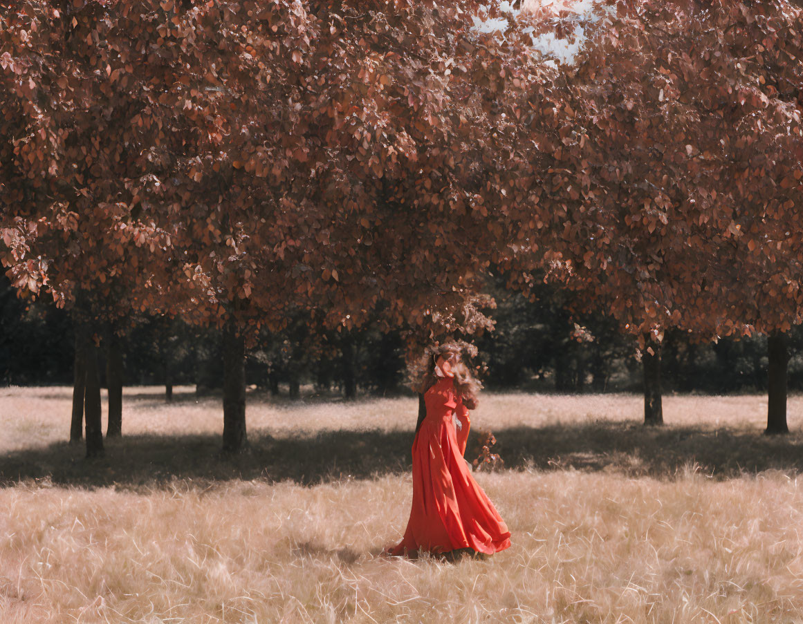 Woman in red dress with flower crown walking under autumn trees in sunlit meadow