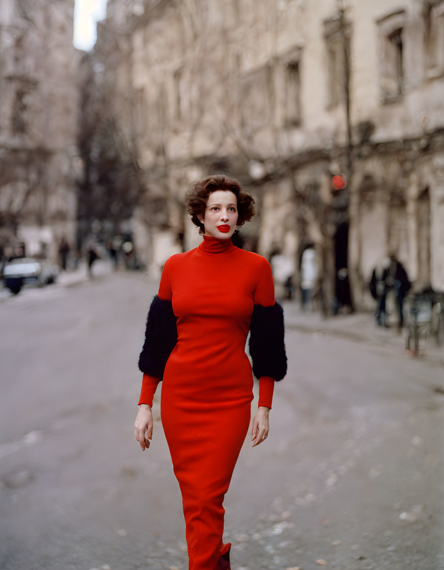 Stylish woman in red dress walking in city street with blurred buildings and trees