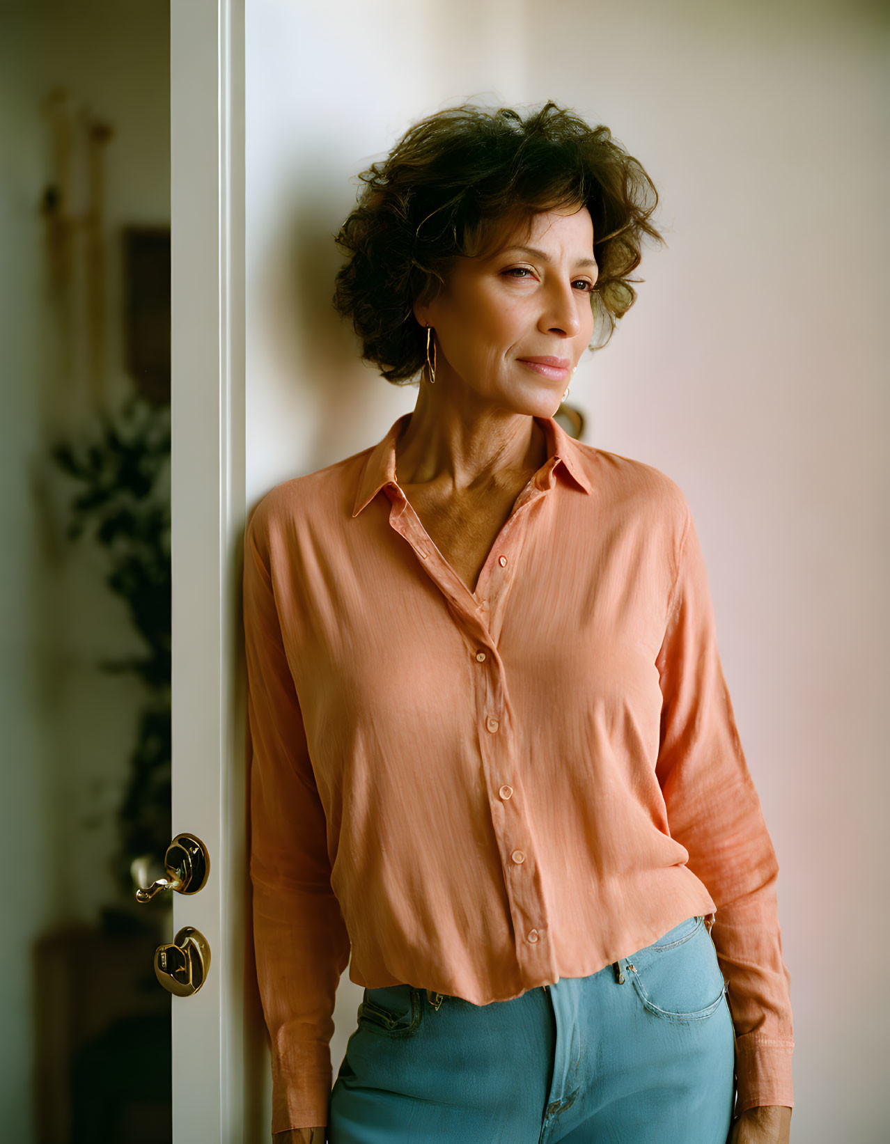 Curly-Haired Older Woman in Salmon Pink Shirt Standing by Open Door