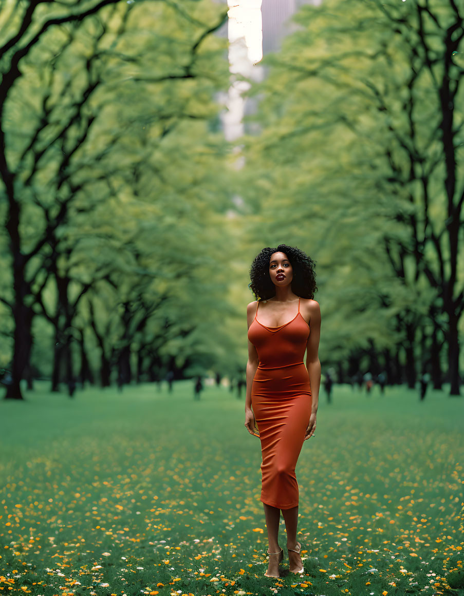 Woman in red dress on grassy path surrounded by trees and yellow flowers.