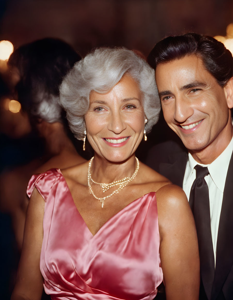 Sophisticated older woman in pink satin dress with man in black suit and tie