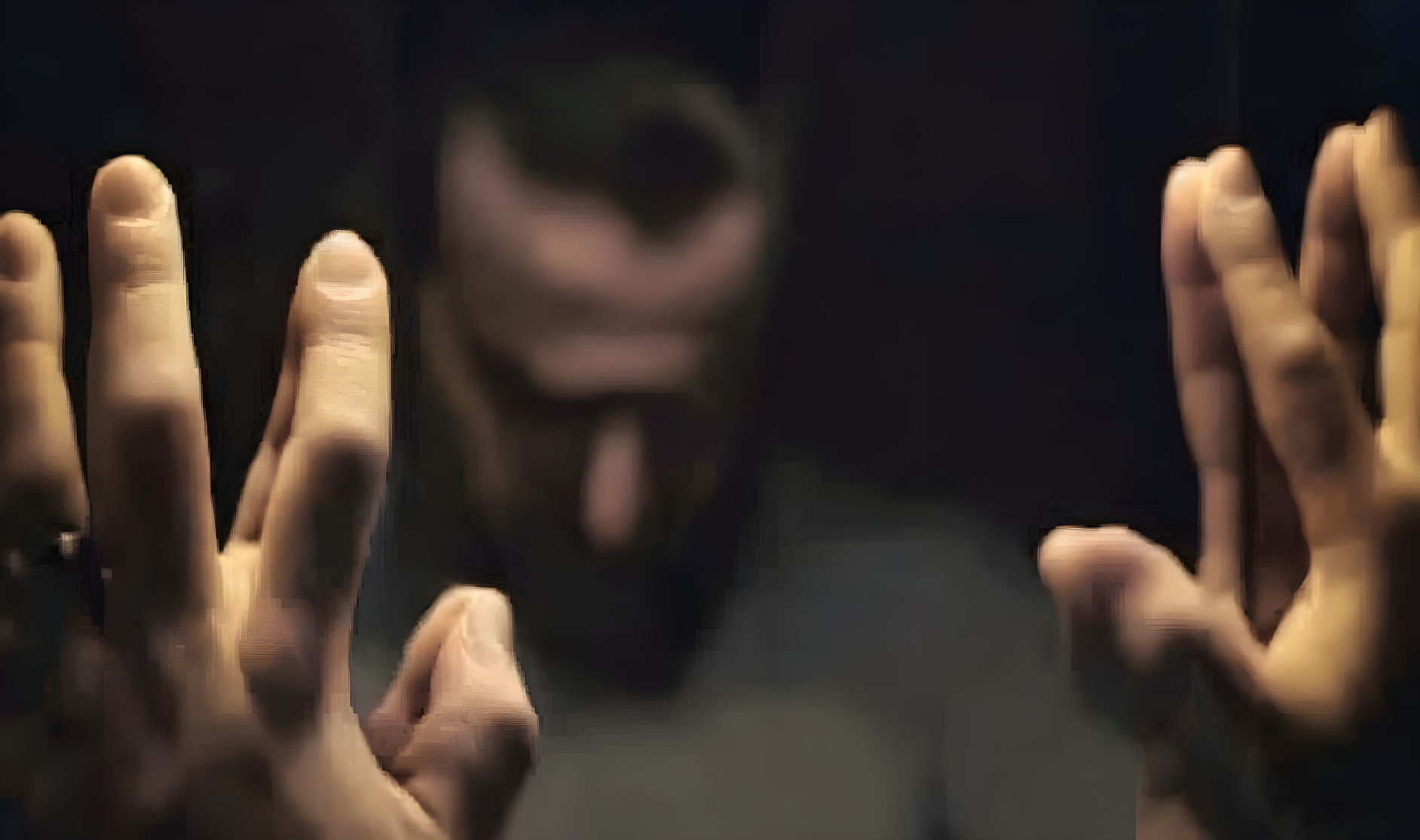 Blurred person with beard gesturing hands in dimly lit background