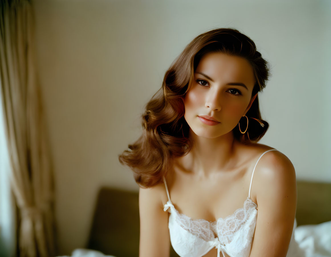 Styled hair, hoop earrings, white lace top: Elegant woman poses in softly lit room