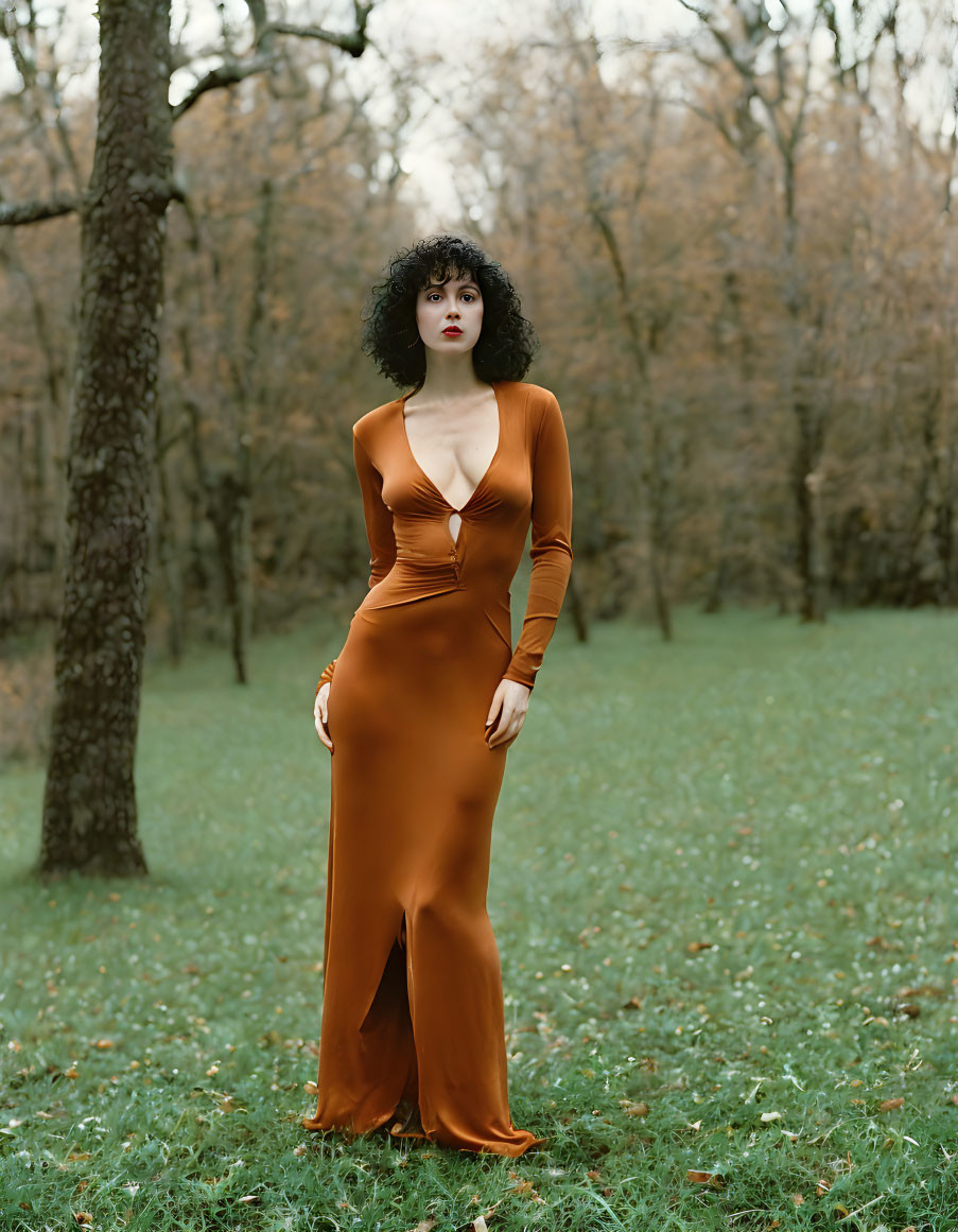 Curly-haired woman in brown dress at park with autumn trees