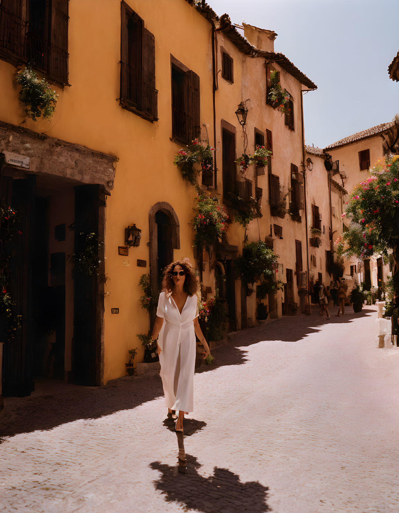 Woman in white dress strolling past yellow buildings on charming street