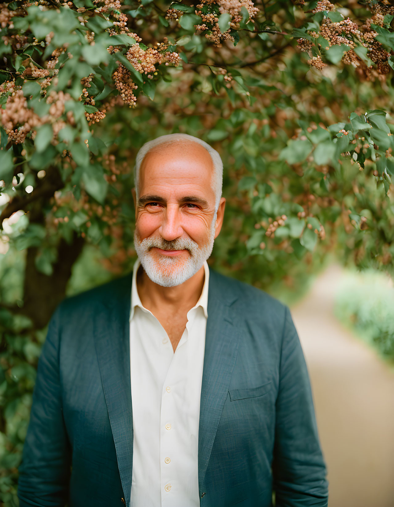 Smiling man in blue blazer and white shirt against green foliage