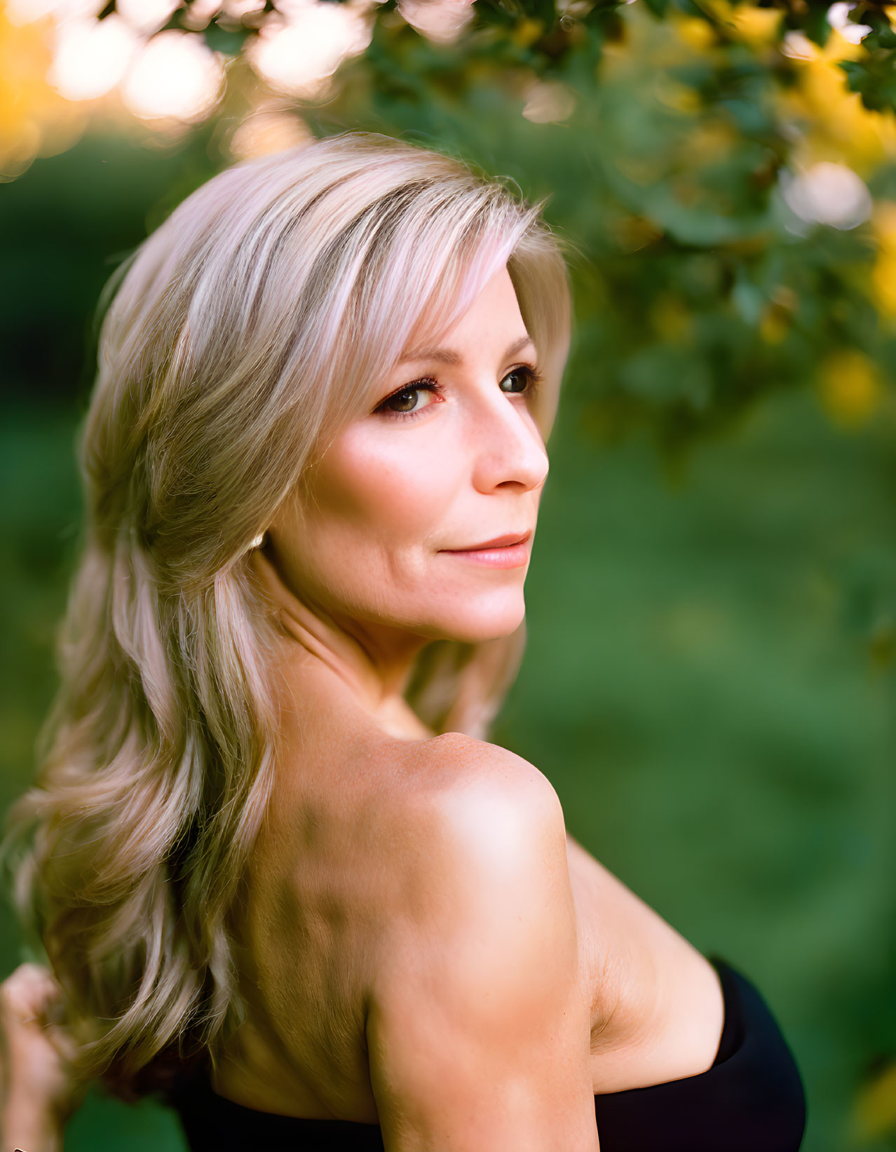 Blonde woman gazes over shoulder in green background.