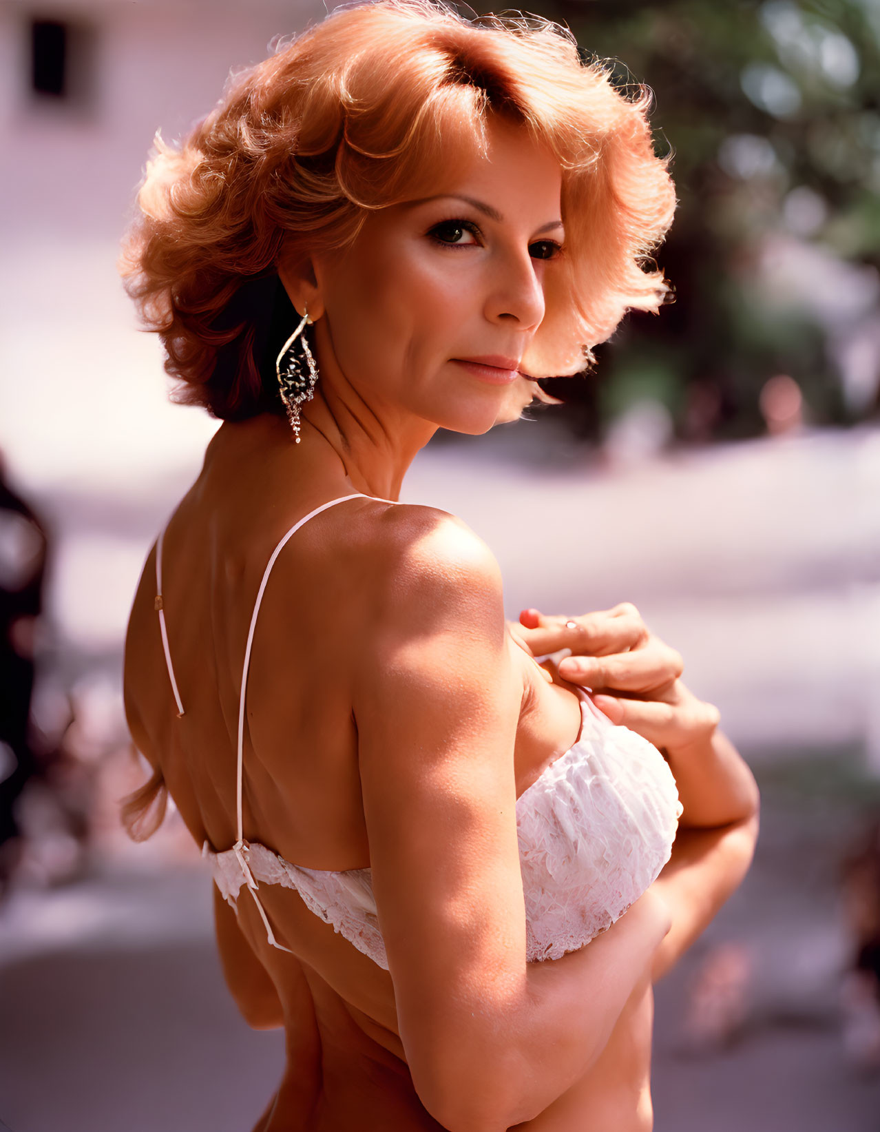 Red-haired woman in white lingerie and drop earrings posing elegantly