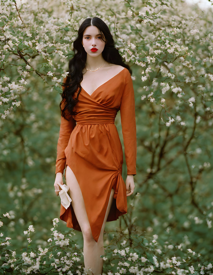 Woman in burnt orange dress among white blossoming bushes