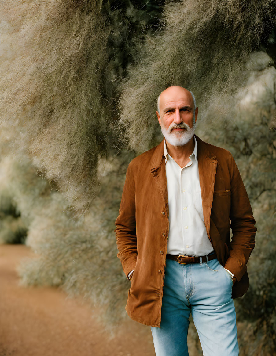 Bearded man in brown jacket on path with greenery