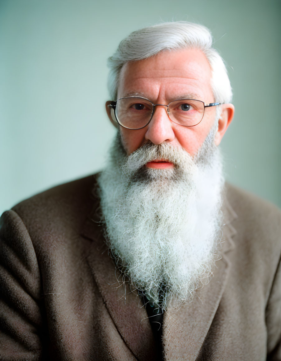 Elderly man in white beard, glasses, brown blazer, dark tie on teal background