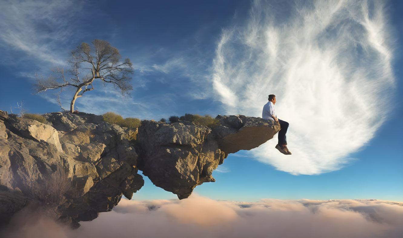 Person sitting on overhanging rock cliff above lone tree and blue sky