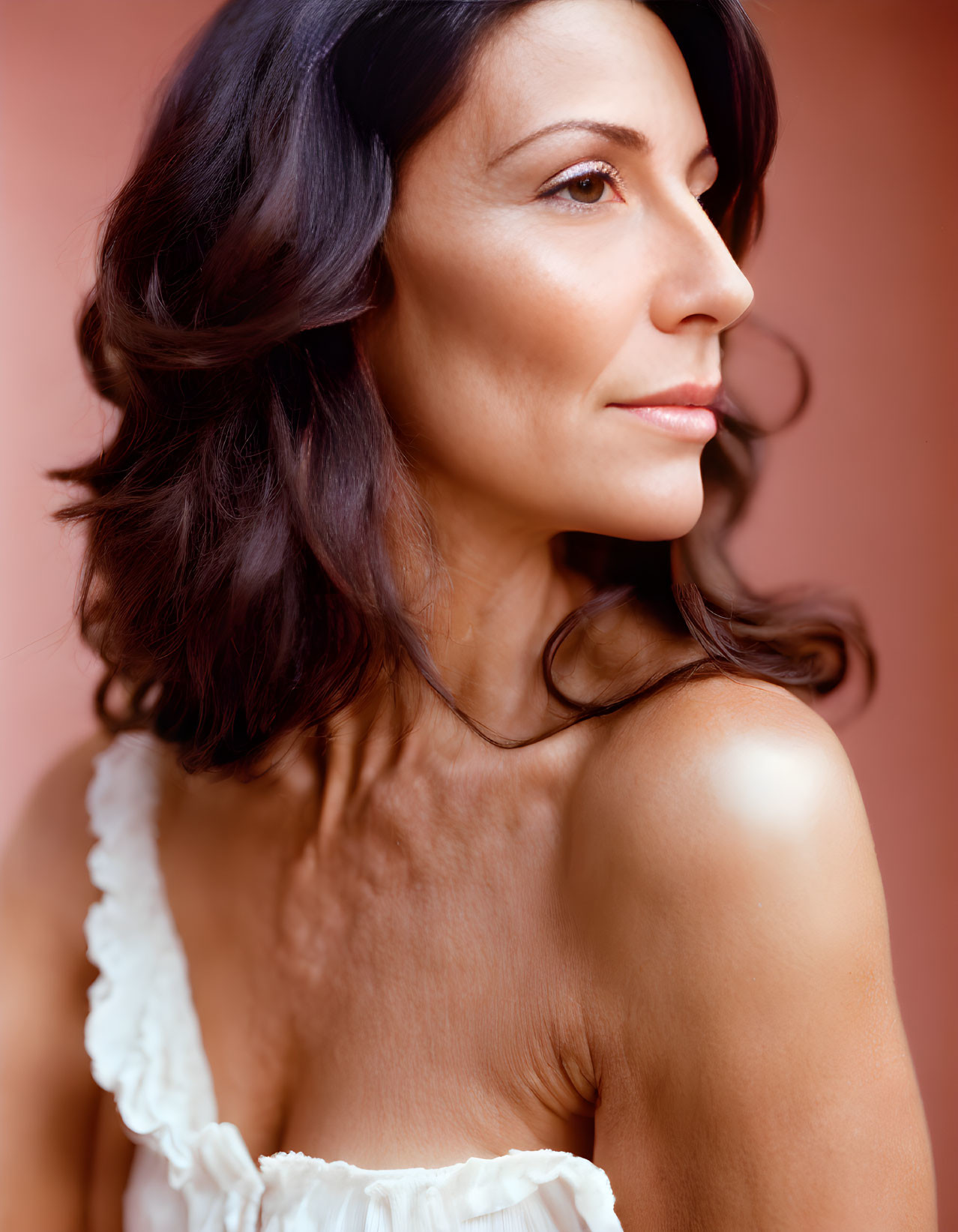 Dark-haired woman in white ruffled garment on warm background