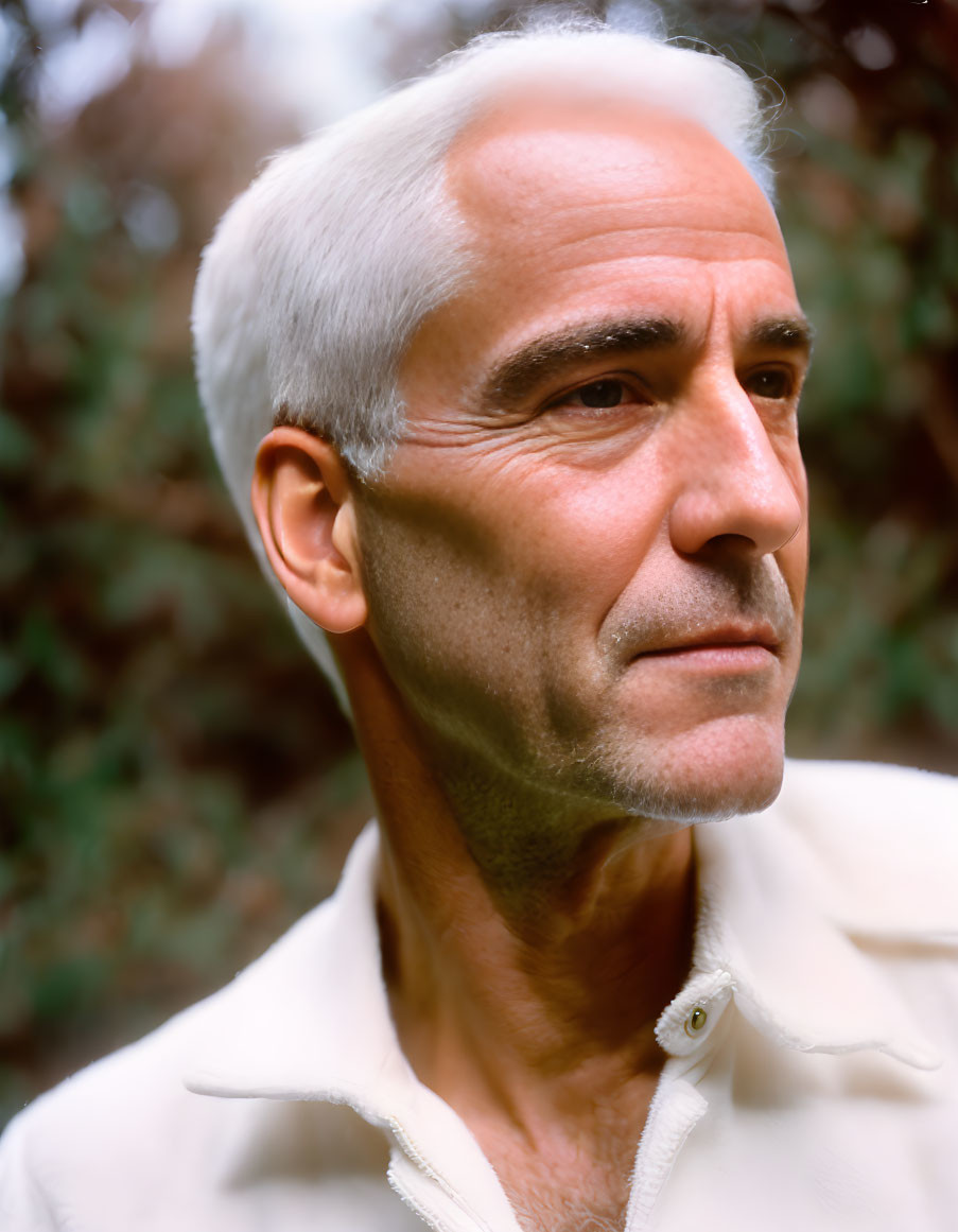 Elderly man portrait with grey hair and thoughtful expression, light shirt, greenery background