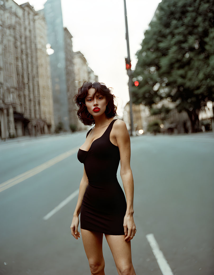 Woman in black dress on urban street with red traffic light